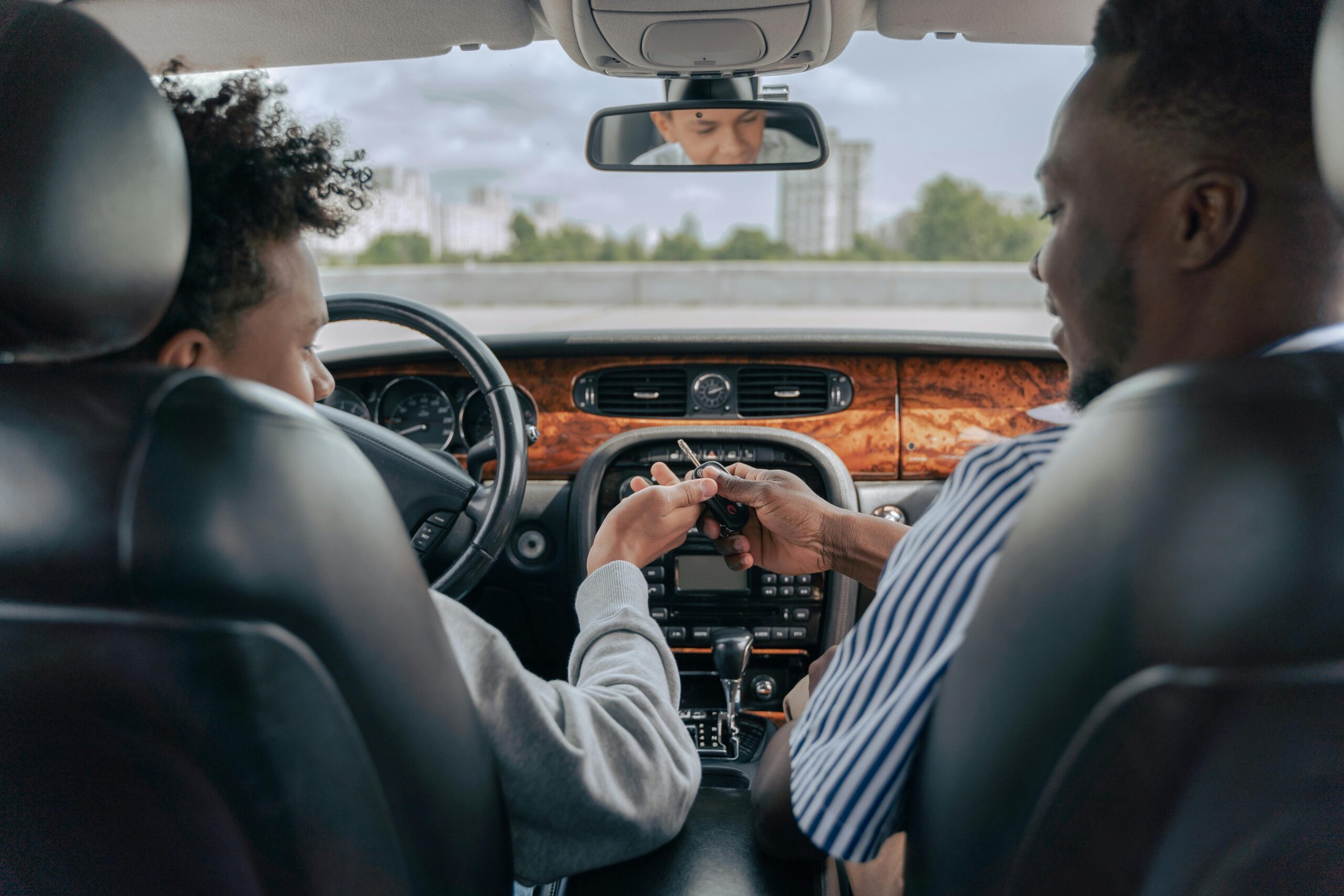 Man handing car keys to his son while sitting in the car.