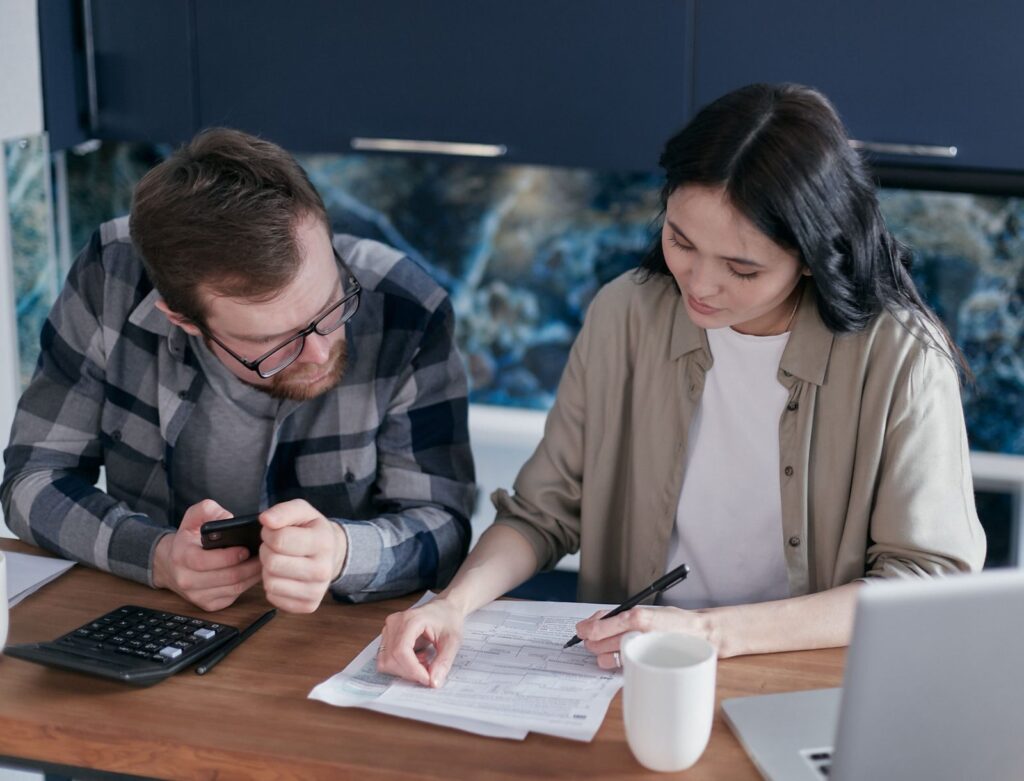 How does insurance work — couple reviewing paperwork at their kitchen table with a calculator and laptop
